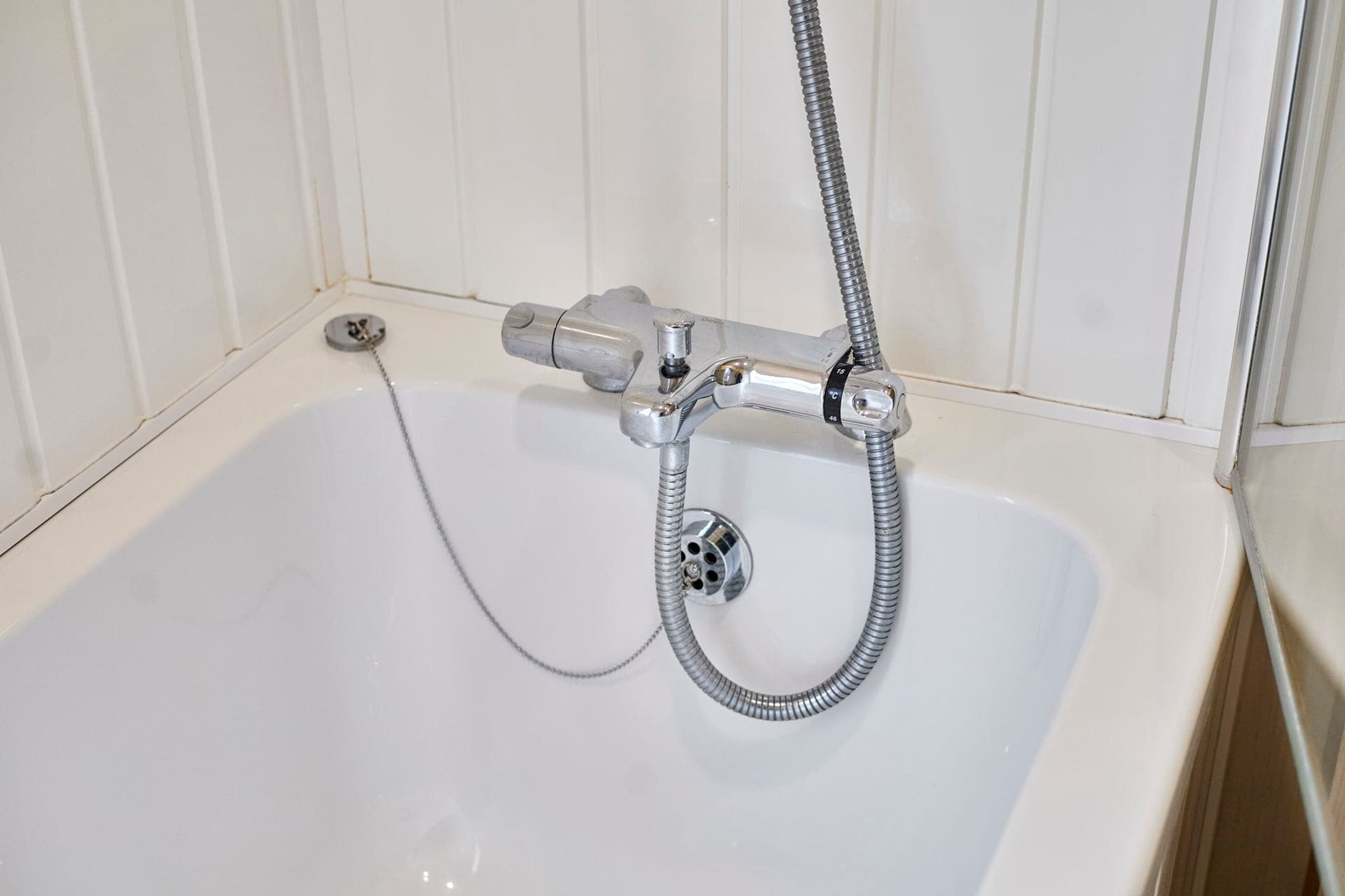 Une baignoire blanche avec un robinet et un tuyau en chrome.
