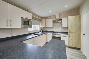 A modern kitchen with a dark countertop, stainless steel appliances, and light-colored cabinetry. - Host Stay Rowan Lodge (Malton)