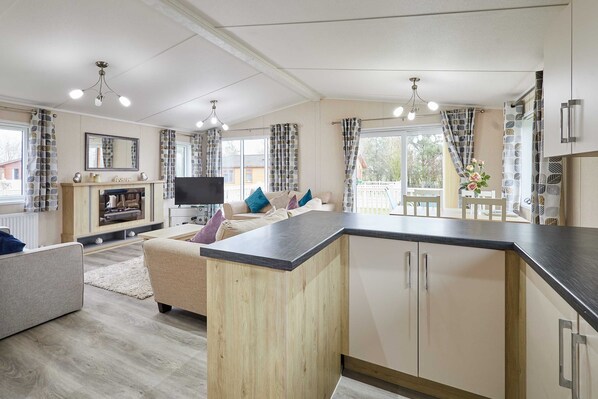 A modern kitchen with a central island, wooden cabinets, and a built-in TV. - Host Stay Rowan Lodge (Malton)