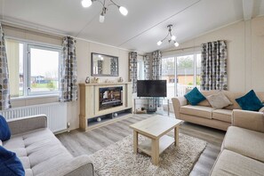 A living room with a sofa, a coffee table, a TV, and a fireplace. - Host Stay Rowan Lodge (Malton)