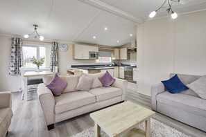 A modern living room with a sofa, a coffee table, and a dining area with a table and chairs. - Host Stay Rowan Lodge (Malton)