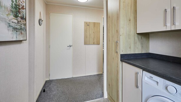 A laundry room with a washing machine, wooden cabinets, and a door leading to another room. - Host Stay Rowan Lodge (Malton)