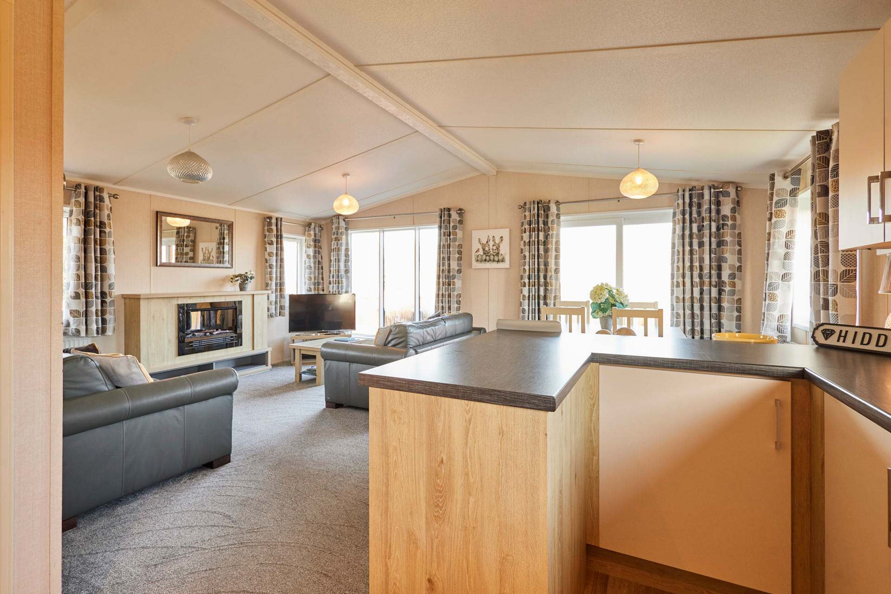 A modern living room with a sofa, a TV, and a fireplace. There is a kitchen area with a counter and cabinets.