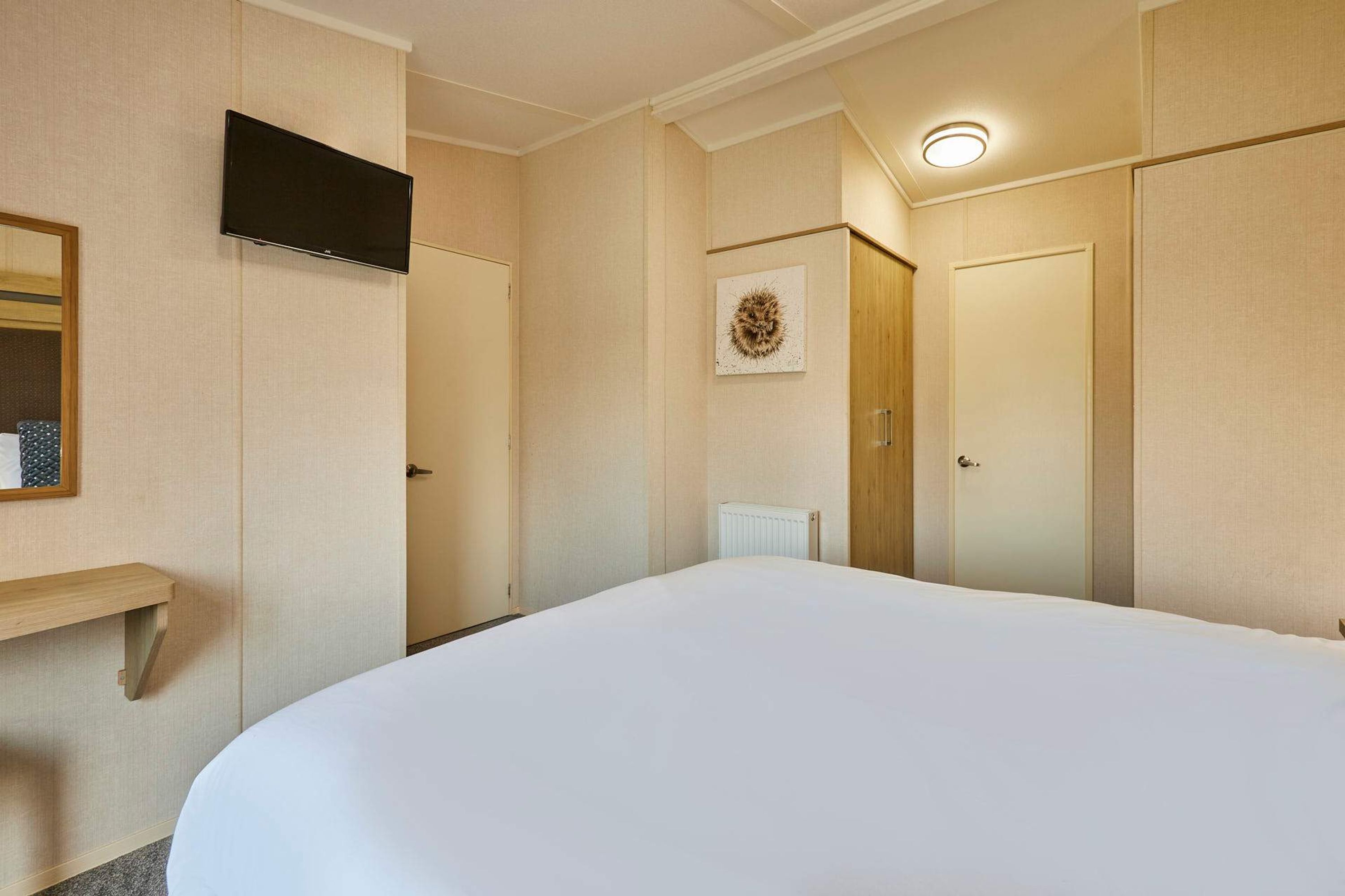 A hotel room with a large bed, a flat-screen TV mounted on the wall, a small shelf, and a radiator.