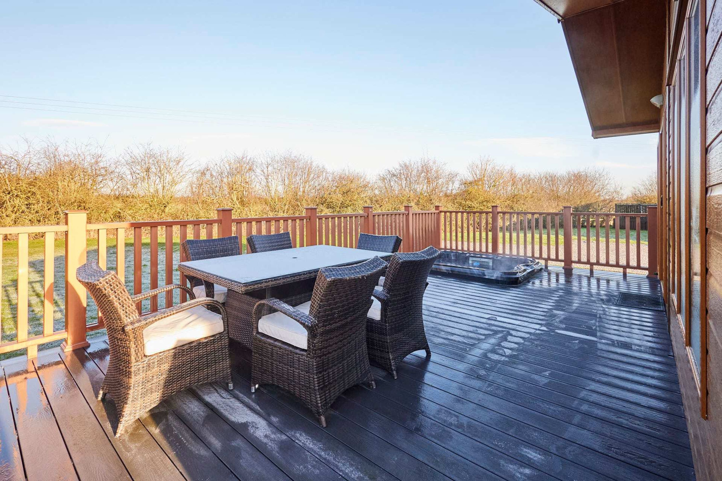 Terraza exterior con mesa y sillas, un jacuzzi y un cerco de madera.