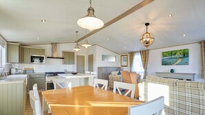 A spacious kitchen with a dining area, a large wooden table, and a cozy seating area with a sofa and cushions. - Host Stay Hedgerow Lodge (Malton)