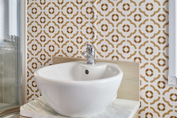 Une salle de bain avec un lavabo blanc, un miroir et un papier peint à motifs.