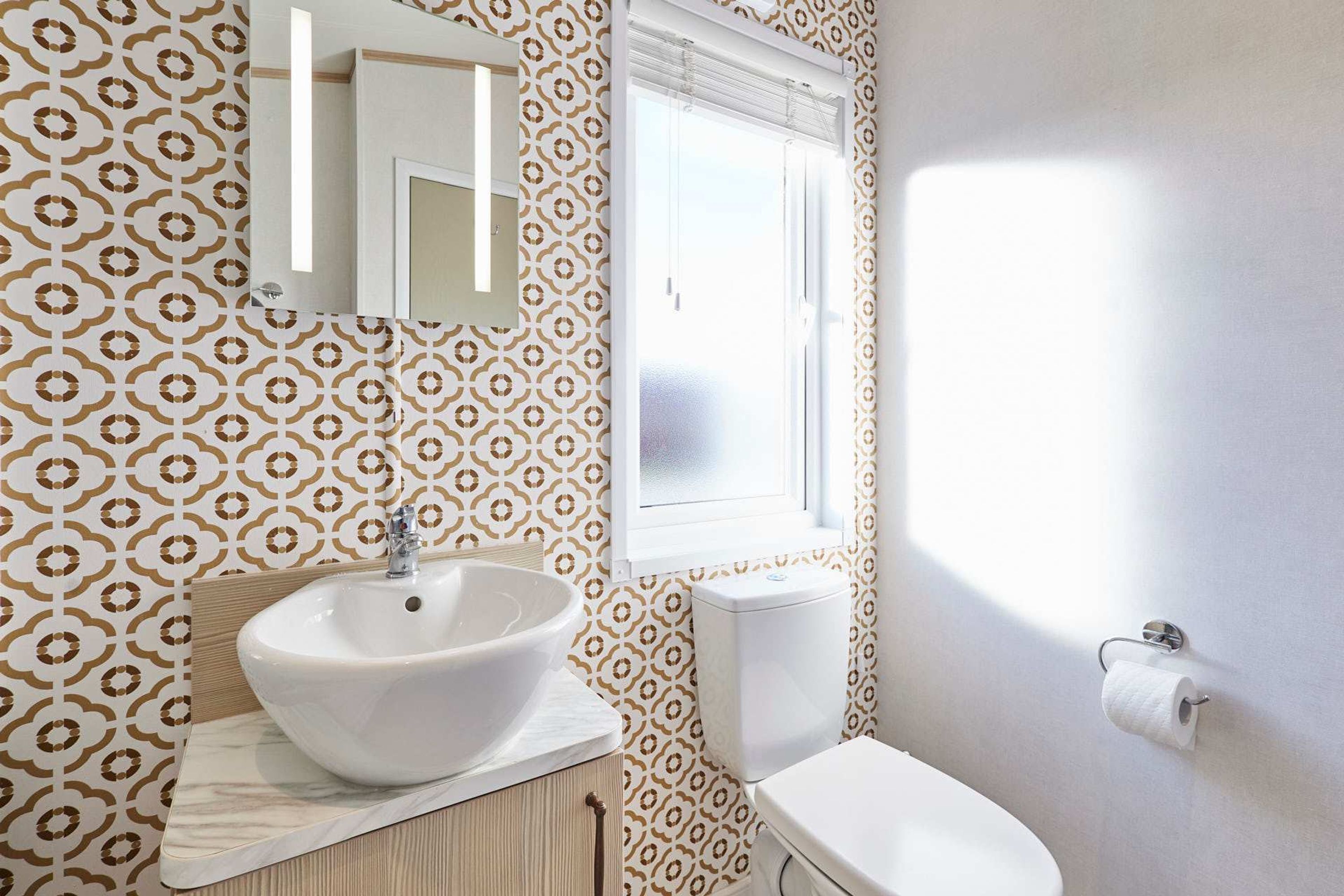 Ein Badezimmer mit einem weißen Waschbecken, einem Spiegel, einer Toilette und Wandpapier mit Muster.