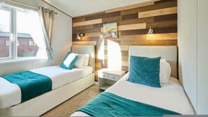 A room with two beds, a nightstand, a wall-mounted painting, and a window with curtains. - Host Stay Hedgerow Lodge (Malton)