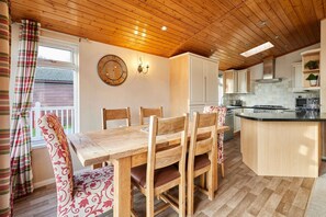 A wooden dining table with four chairs, a kitchen area with cabinets and a stove, and a window with curtains. - Host Stay Crystal Lodge (Malton)