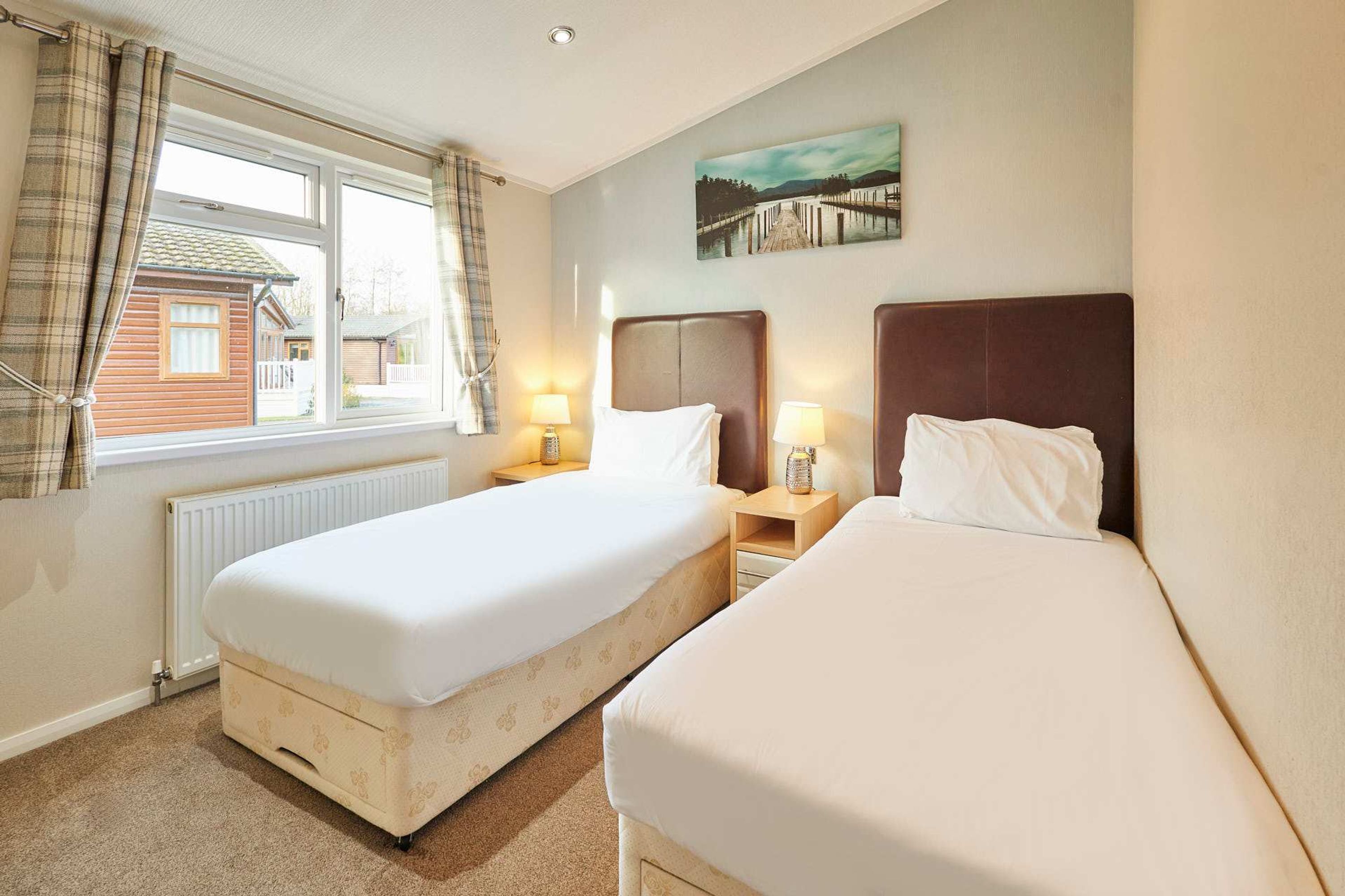 A hotel room with two beds, a window with curtains, a radiator, and a painting on the wall.