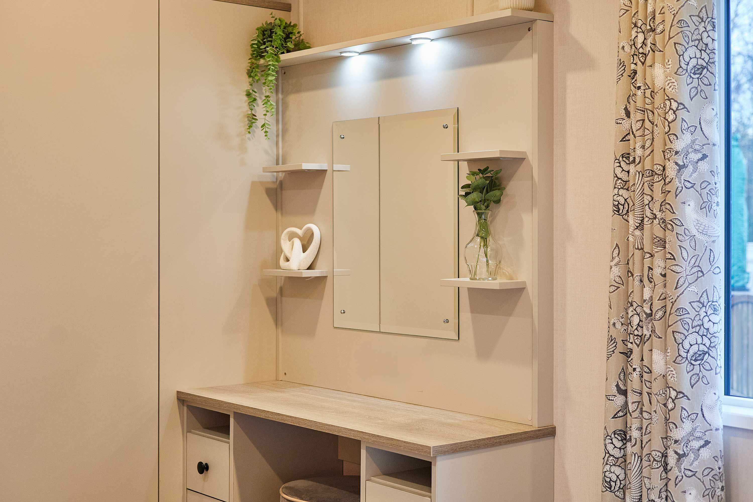 A bedroom with a bed, a bedside table, a dresser, a mirror, and a window with curtains.