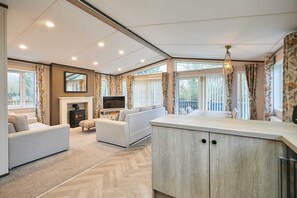 Een moderne woonkamer met een open haard, banken, een televisie en een groot raam met gordijnen.