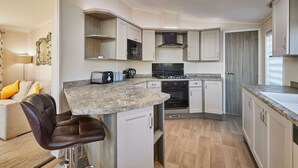 A compact kitchen with white cabinetry, a marble countertop, and a black stove. - Host Stay Penny Lodge (York)