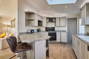 A compact kitchen with white cabinetry, a marble countertop, and a black stove. - Host Stay Penny Lodge (York)