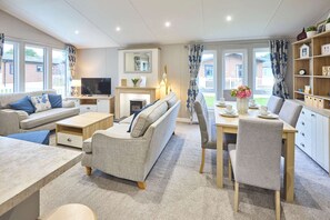 A modern living room with a sofa, coffee table, TV, fireplace, dining table, chairs, and a bookshelf. - Host Stay The Haven Lodge (York)