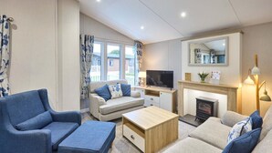 Ein Wohnzimmer mit Sofa, Sessel, Fernseher, Kamin und einem Spiegel an der Wand.
