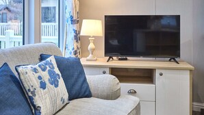 Ein Wohnzimmer mit einer Couch, einem Flachbildfernseher auf einem Holzboden, einer Lampe und Blick ins Freie.