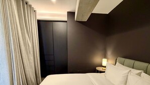 Una habitación de hotel con una cama grande, una mesita de noche con lámpara y un armario de color oscuro.