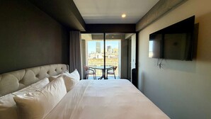 Una habitación de hotel con una cama grande, un televisor montado en la pared y un balcón con mesa y sillas.