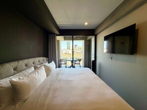 A hotel room with a large bed, a TV mounted on the wall, and a balcony with a table and chairs. - w Charming 2BR w Balcony in Tabacalera (Mexico City)
