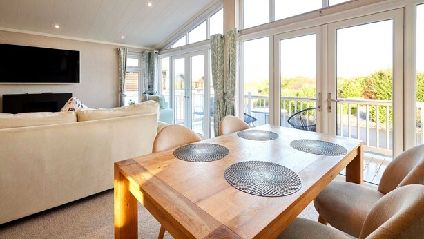 A spacious living area with a wooden dining table, a sofa, and a TV mounted on the wall. - Host Stay Deneb Lodge (Malton)