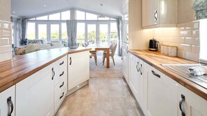A modern kitchen with white cabinets, wooden countertops, and a dining area with a table and chairs. - Host Stay Deneb Lodge (Malton)