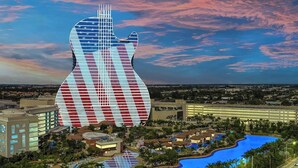 Un grand bâtiment dont la façade a la forme d’une guitare, entouré d’un complexe hôtelier avec des piscines et des palmiers.