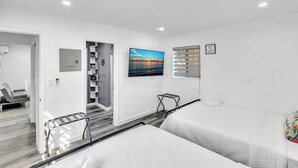 Une chambre d’hôtel moderne, avec un lit, un tableau représentant un coucher de soleil, une fenêtre avec des stores et un escalier menant à une autre pièce.