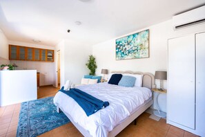 A bedroom with a bed, bedside tables, a nightstand, a painting, a wardrobe, and a kitchen area. - 5BR Family Retreat Spa, Sauna, Gym Miranda sleep12 (Miranda)