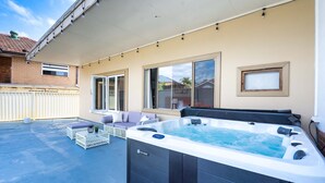 Een overdekt terras met een jacuzzi, zitplaatsen buiten en grote ramen.
