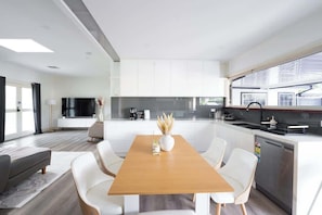 A modern kitchen with white cabinets, a wooden dining table, and a view of the street.