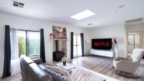 Een moderne woonkamer met een bank, een fauteuil, een open haard, een televisie en een groot raam.