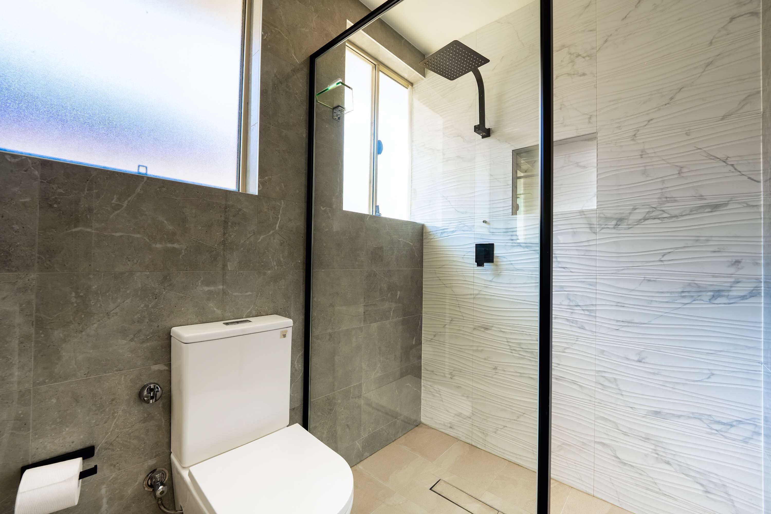 A modern bathroom with a toilet, a shower, and a glass partition.