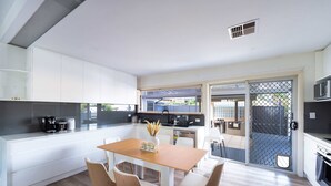 Een moderne keuken met witte kastjes, een eettafel met stoelen en uitzicht op de achtertuin via een schuifdeur.