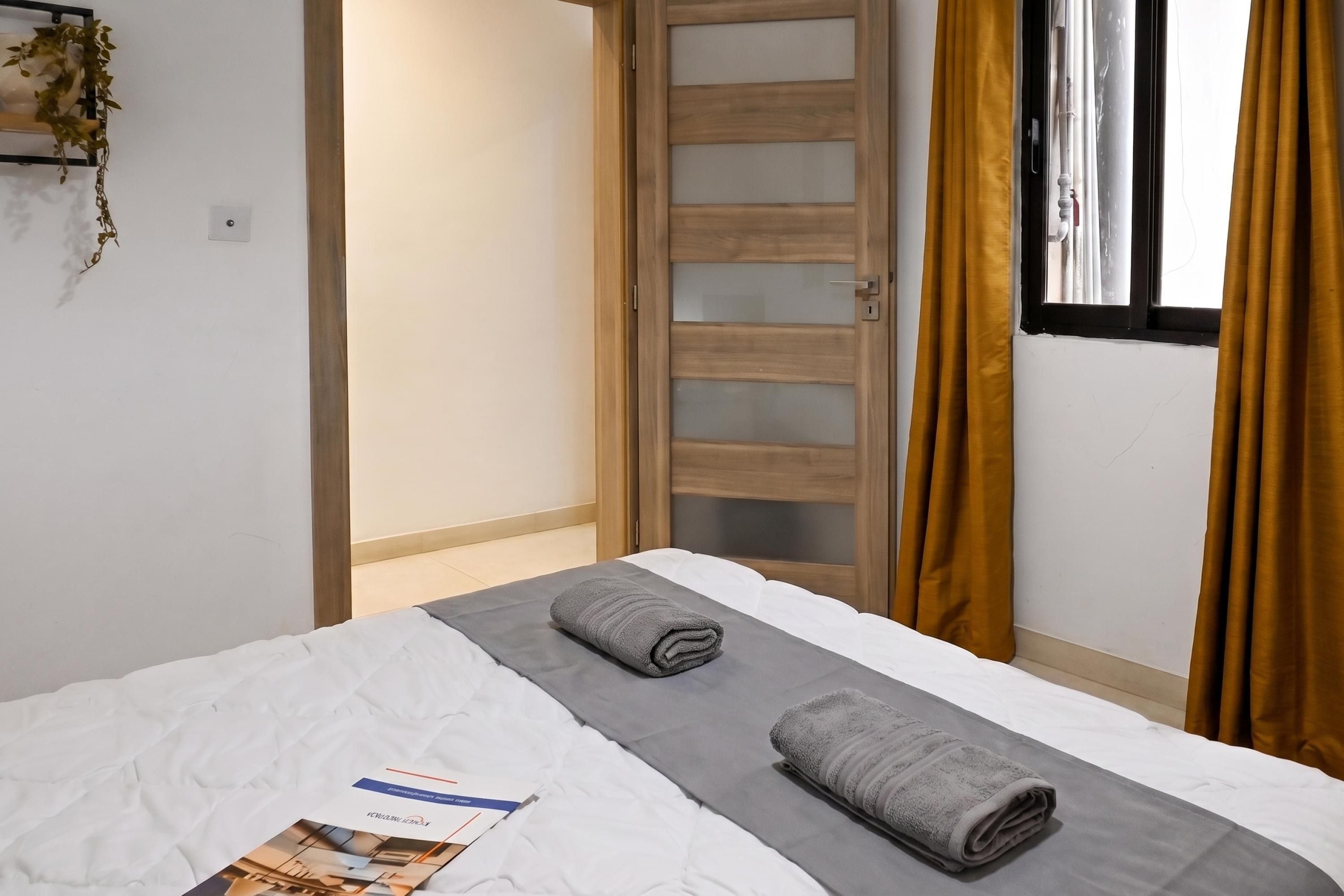 Ein Hotelzimmer mit einem Bett, einem Fenster mit Vorhängen und einer Tür mit einer blickdichten Glasscheibe.