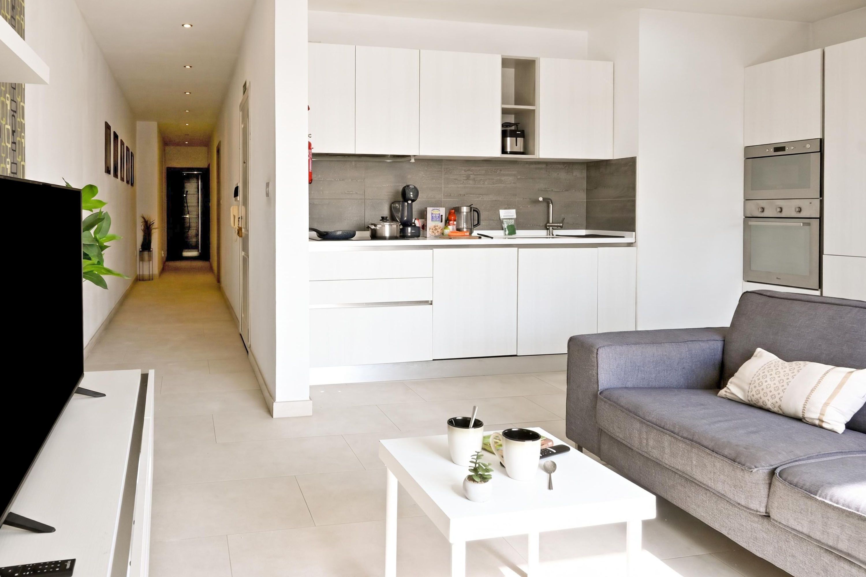 A modern kitchen with white cabinetry, a built-in oven, and a countertop with various appliances.