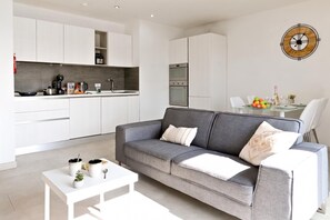 A modern living space with a grey sofa, white coffee table, and a dining area with a glass table. - A Sunny Seaview In Central Sliema (Sliema)