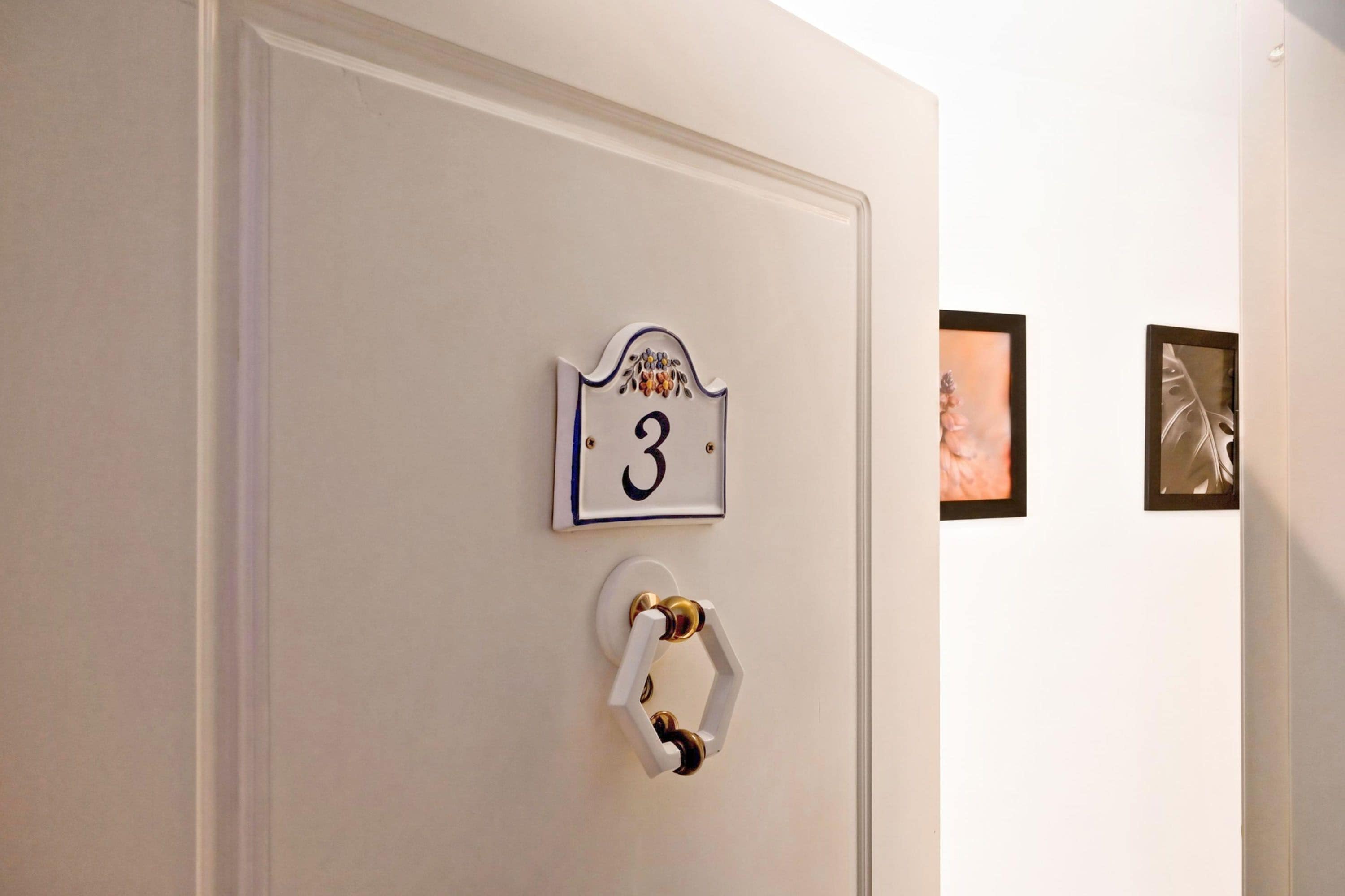 A door with a number plate indicating room 3, a door handle, and two framed pictures on the wall.