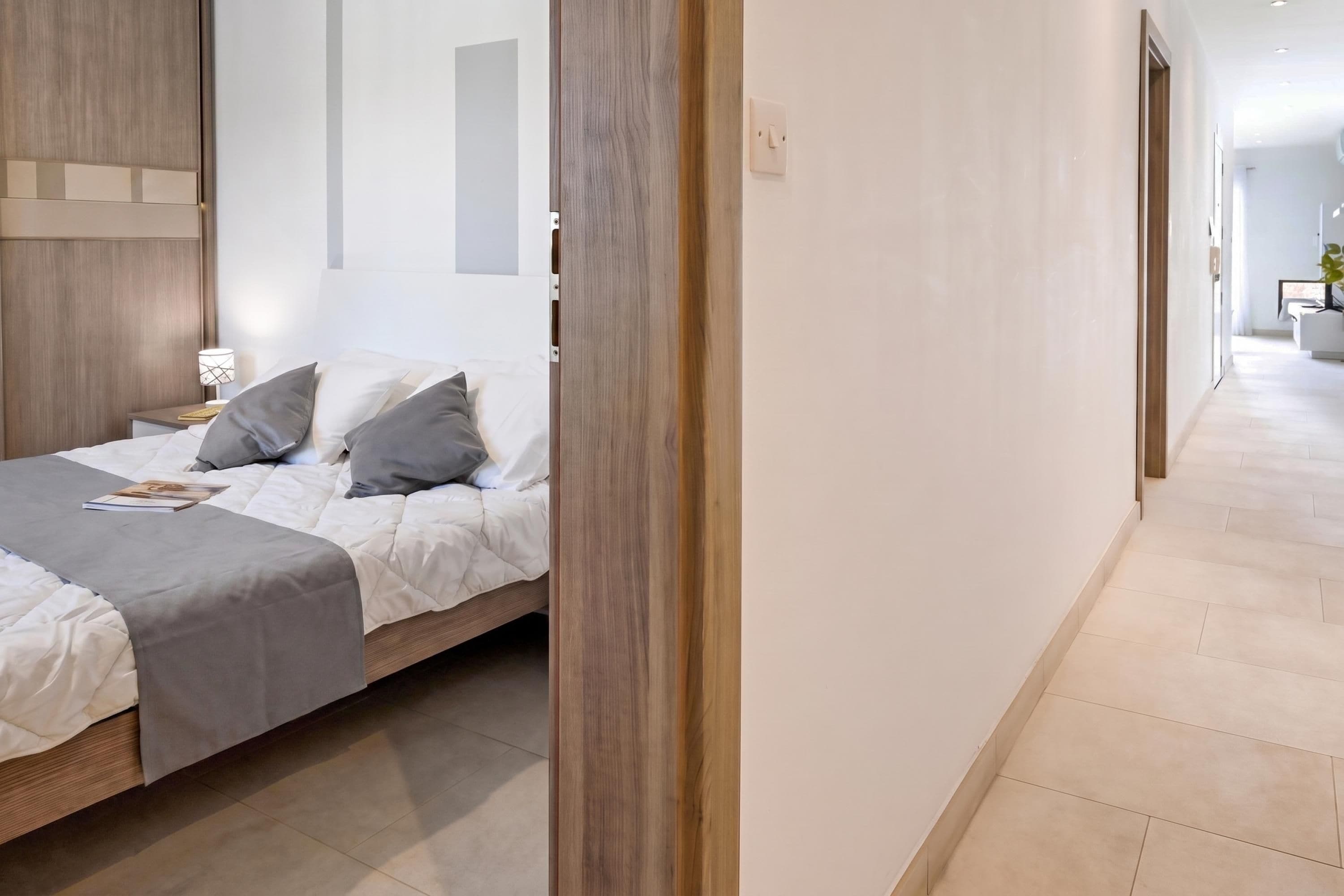 Ein modernes Schlafzimmer mit einem Holzbettgestell, einem Nachttisch mit Lampe und Blick in einen Flur.