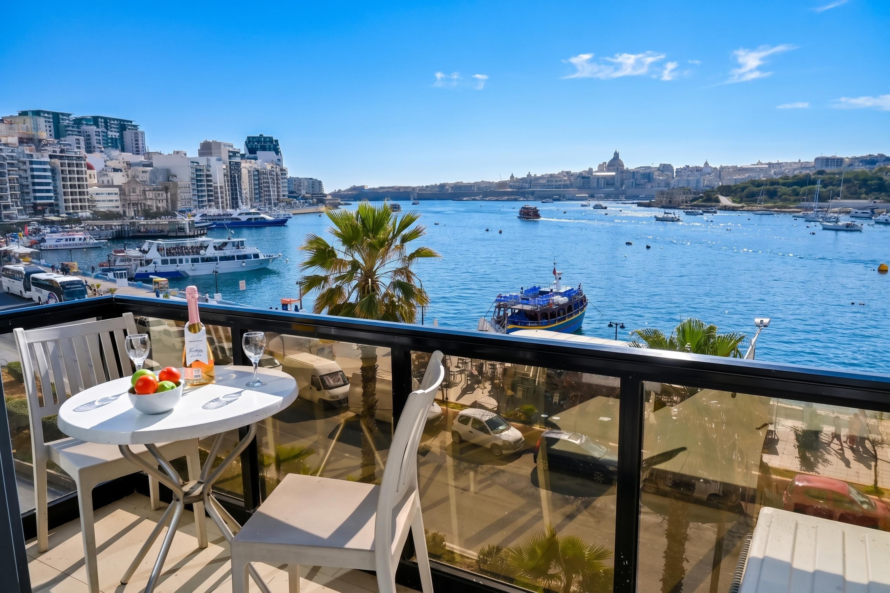 Un balcón con mesa, sillas y vistas a un puerto deportivo con barcos y edificios de la ciudad.