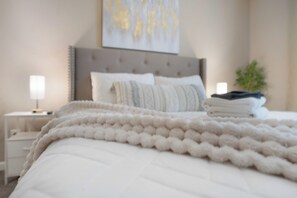 A neatly made bed with a fluffy white blanket, a bedside lamp, and a folded towel on the nightstand. - Smithson Stay-Wi-Fi|King Bed | Desk | Private Bath in Each Room (Clarksville)