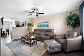 A modern living room with a sofa, ottoman, coffee table, and a ceiling fan. - Smithson Stay-Wi-Fi|King Bed | Desk | Private Bath in Each Room (Clarksville)