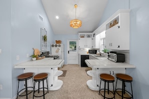 A kitchen with white cabinets, a central island with stools, a hanging light fixture, and a door leading to a garden.