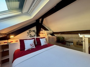 A bedroom with a sloped ceiling, a bed with red and white bedding, a wall-mounted air conditioner, and a skylight. - "Do small things with love" (Lisboa)