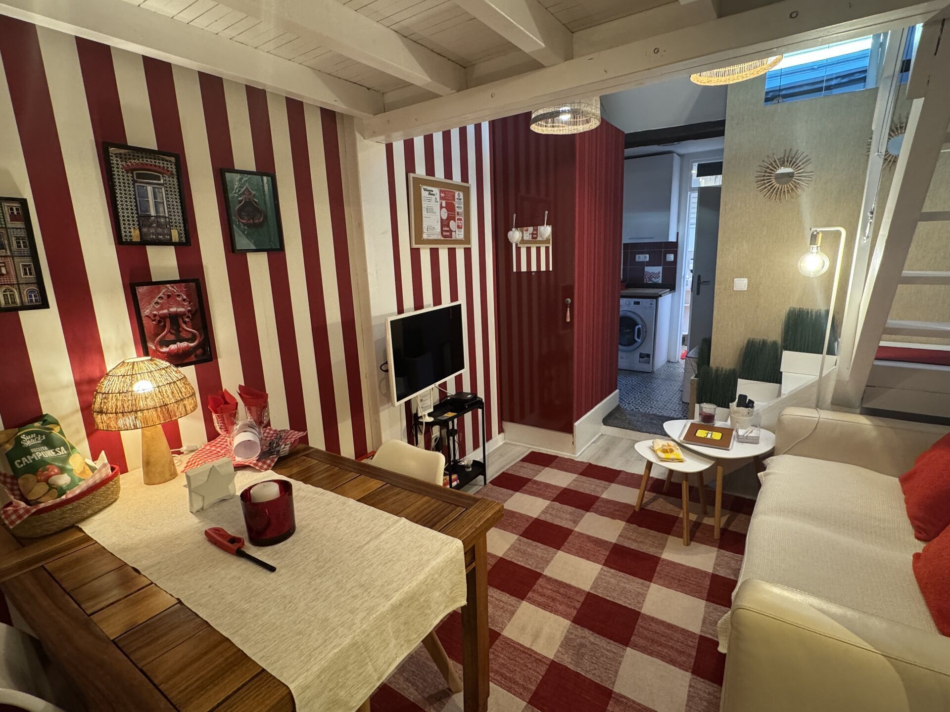A room with a checkered floor, striped walls, a dining table with a lamp, a TV, and a sofa.