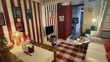 A room with a checkered floor, striped walls, a dining table with a lamp, a TV, and a sofa.