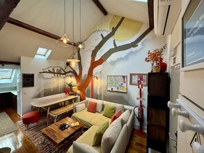 Ein gemütliches Wohnzimmer mit einer großen Wandmalerei eines Baumes, einem Holztisch, einer Couch und einem Essbereich.