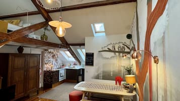 A loft-style room with exposed wooden beams, a dining area with a checkered tablecloth, and a mural on the wall.
