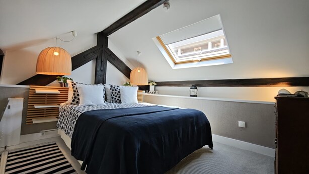Een slaapkamer met een bed, dakraam, bureau en hanglamp.